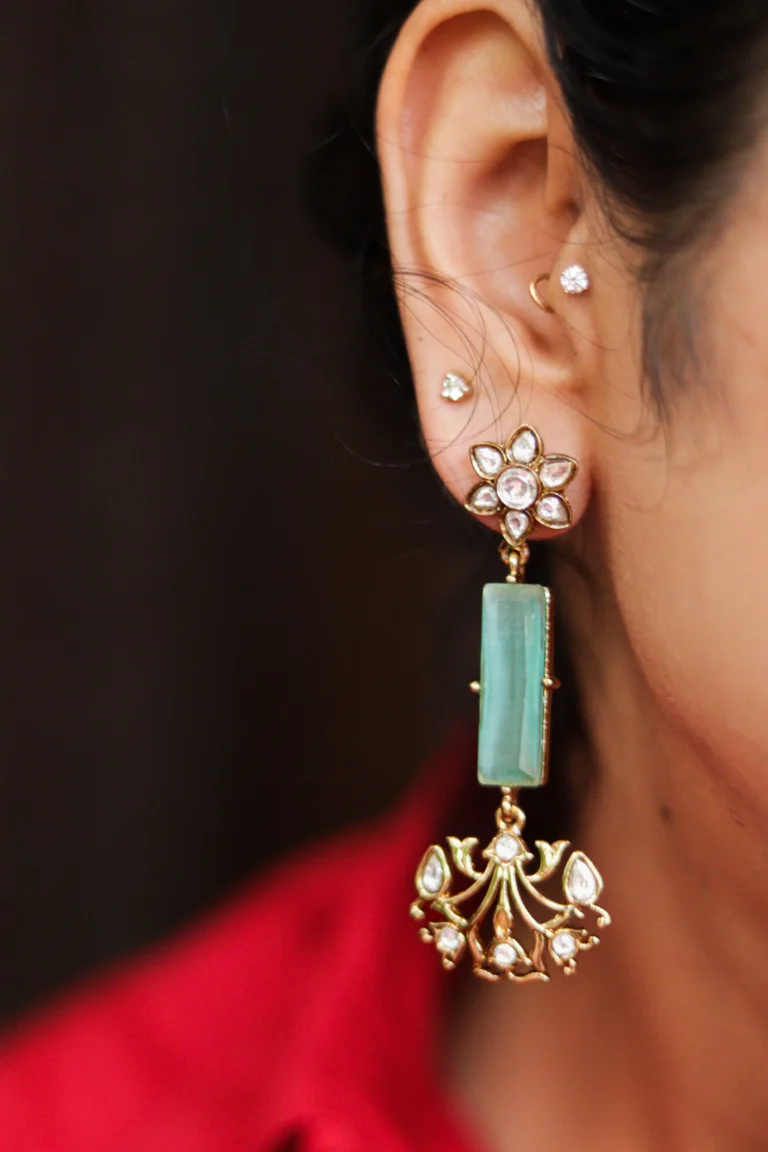 Close-up of woman wearing gold-plated Mehfil Earrings with green stone and kundan floral design by Twilight by Twinkle